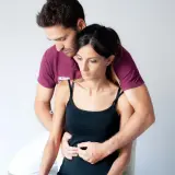 Un terapista esegue un massaggio diaframma su una donna, con le mani posizionate sull'addome per favorire il rilassamento e la respirazione profonda.