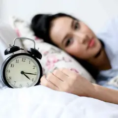 Svegliarsi alle 4 è un momento chiave per il benessere secondo la medicina cinese. La donna nella foto è a letto, con una sveglia che segna le 4.
