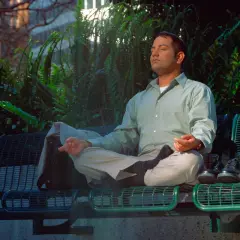 Uomo in meditazione su una panchina, con un atteggiamento zen. Le mani in posizione di preghiera, gli occhi chiusi, circondato dal verde.