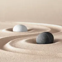 Due pietre, una bianca e una nera, su sabbia rastrellata, evocano il simbolo bianco e nero tao significato di equilibrio e dualità.