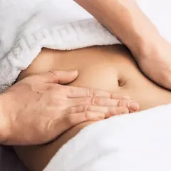 Hands massaging a person's abdomen, covered by a white towel.