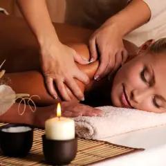 Mani esperte eseguono un massaggio corpo a corpo rilassante. Una candela accesa e decorazioni naturali creano un'atmosfera di pace.