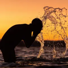 Silhouette of a person splashing water on their face at sunset.