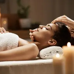 Woman receiving a facial massage in a dimly lit room with candles.