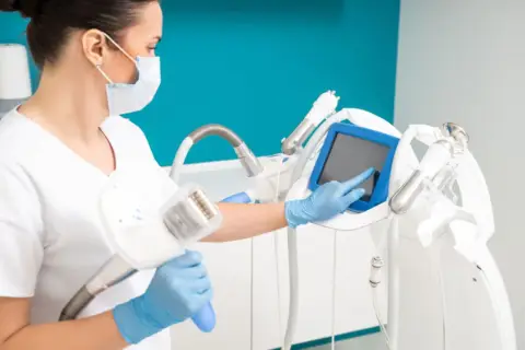 Operatrice con guanti blu e mascherina prepara un macchinario per il massaggio endodermico, toccando lo schermo.