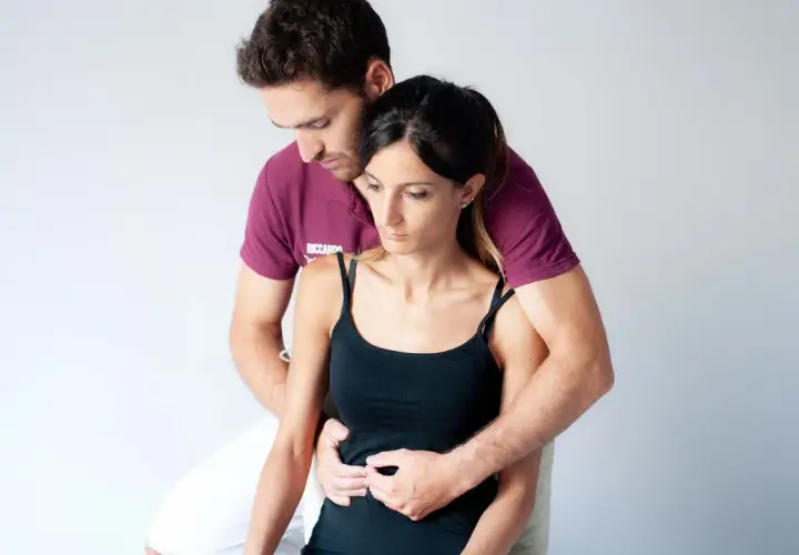 Un terapista esegue un massaggio diaframma su una donna, con le mani posizionate sull'addome per favorire il rilassamento e la respirazione profonda.