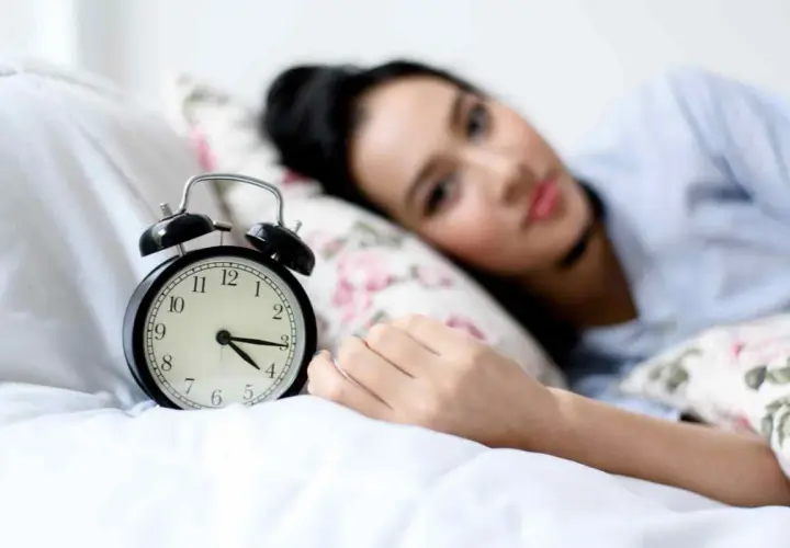 Svegliarsi alle 4 è un momento chiave per il benessere secondo la medicina cinese. La donna nella foto è a letto, con una sveglia che segna le 4.
