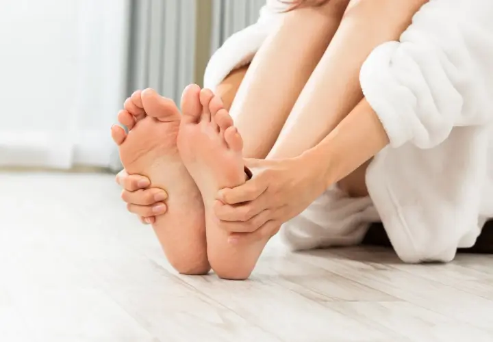 Mani che massaggiano delicatamente i piedi, avvolti in un morbido accappatoio bianco, per un momento di puro relax.