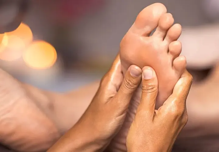 Close-up of hands massaging a foot, with soft, blurred lights in the background.