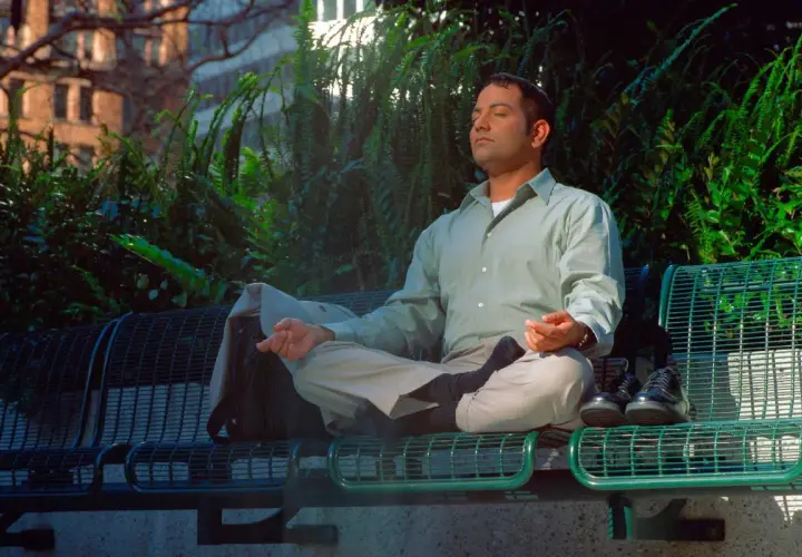 Uomo in meditazione su una panchina, con un atteggiamento zen. Le mani in posizione di preghiera, gli occhi chiusi, circondato dal verde.