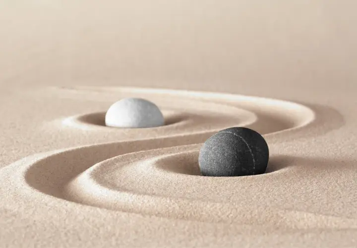 Due pietre, una bianca e una nera, su sabbia rastrellata, evocano il simbolo bianco e nero tao significato di equilibrio e dualità.