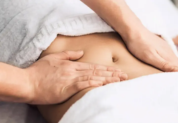 Hands massaging a person's abdomen, covered by a white towel.