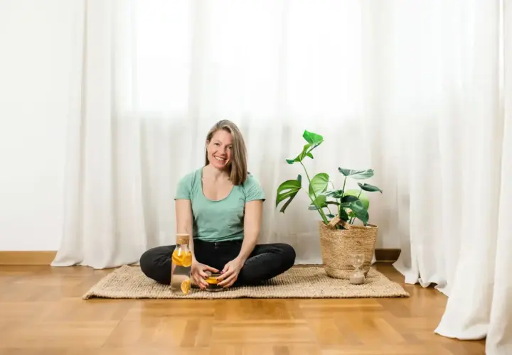 Donna sorridente in posizione yoga, con acqua aromatizzata e una pianta. Un momento di relax, sperando che il suo rene bloccato si risolva presto.