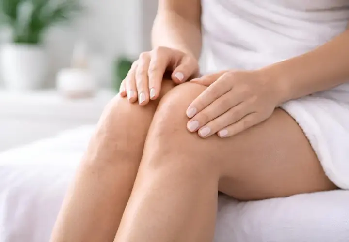 Close-up of a woman's knees and hands, showing skin texture.