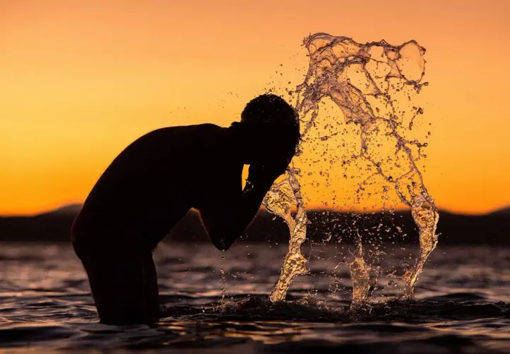 Silhouette of a person splashing water on their face at sunset.
