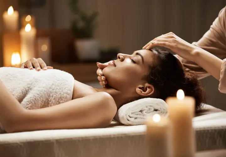 Woman receiving a facial massage in a dimly lit room with candles.