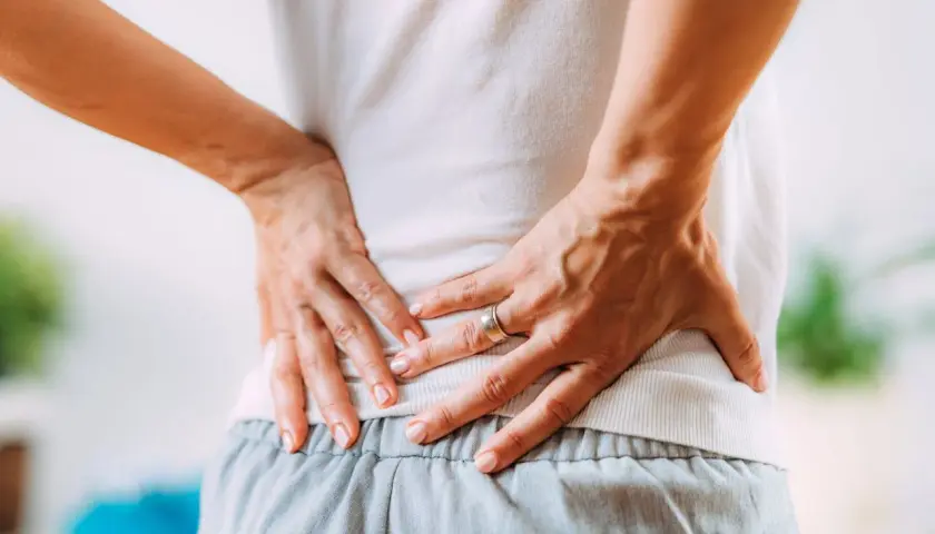 Mani che premono sulla schiena dolente, cercando sollievo nei punti shiatsu per sciatica.