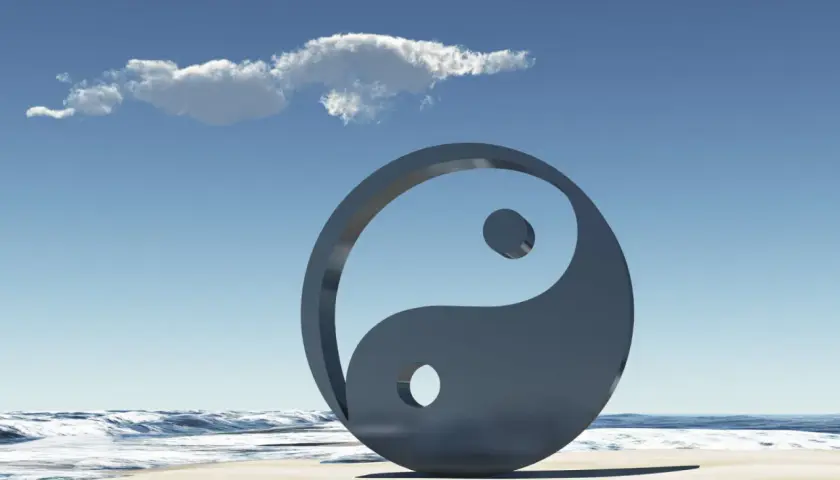 Simbolo Yin e Yang sulla spiaggia, con onde e cielo azzurro. Rappresenta l'equilibrio universale, il yin e yang significato esoterico.
