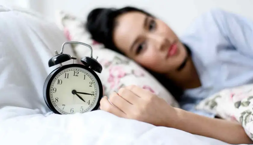 Svegliarsi alle 4 è un momento chiave per il benessere secondo la medicina cinese. La donna nella foto è a letto, con una sveglia che segna le 4.