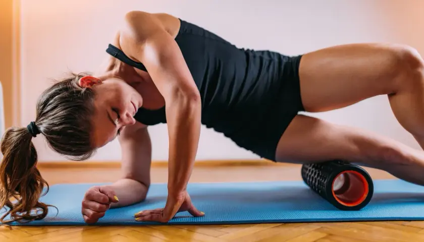 Donna usa un rullo massaggiante per sciogliere la tensione muscolare. A cosa serve il rullo massaggiante? A migliorare il recupero e la flessibilità.