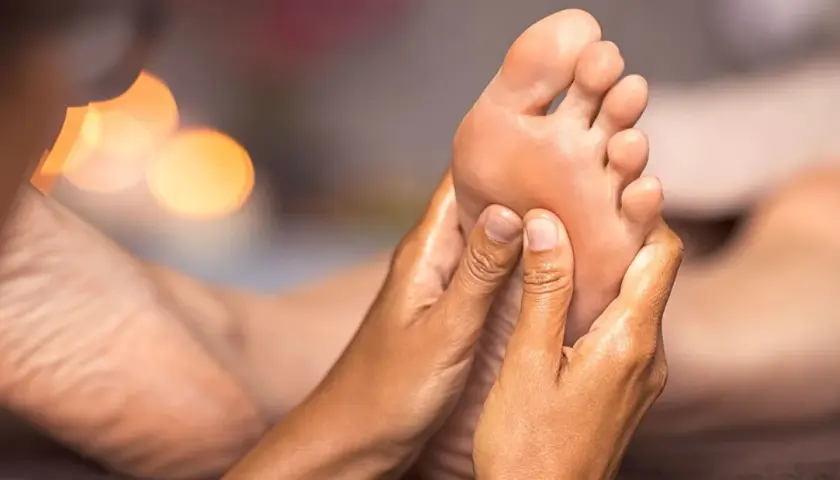 Close-up of hands massaging a foot, with soft, blurred lights in the background.