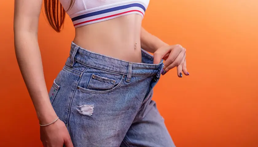 Woman in a crop top and oversized jeans, showing off her slim waist.