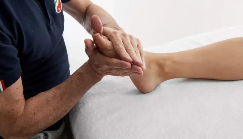 A person's hands massaging a foot on a white towel.