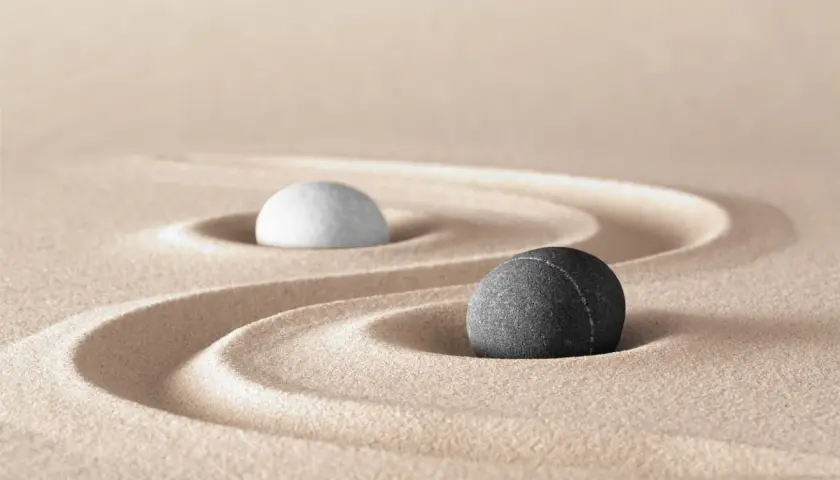 Due pietre, una bianca e una nera, su sabbia rastrellata, evocano il simbolo bianco e nero tao significato di equilibrio e dualità.