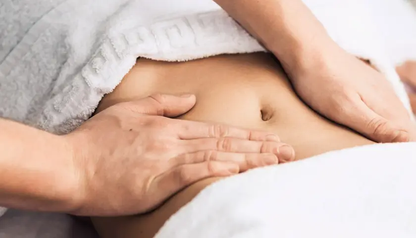 Hands massaging a person's abdomen, covered by a white towel.