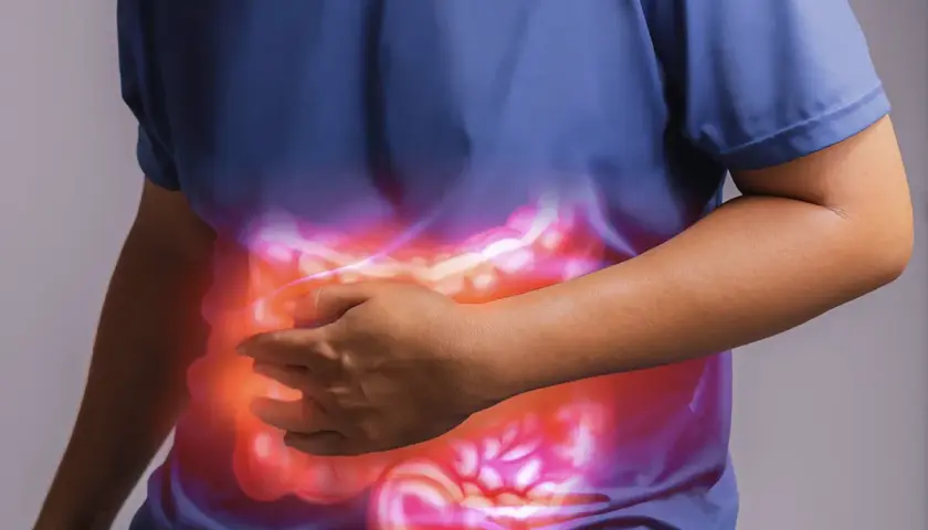 Persona che si tiene la pancia, con un'illustrazione luminosa dell'intestino. Un aiuto per l'automassaggio colon irritabile.