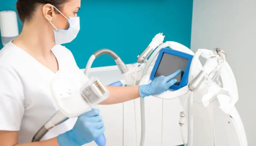 Operatrice con guanti blu e mascherina prepara un macchinario per il massaggio endodermico, toccando lo schermo.