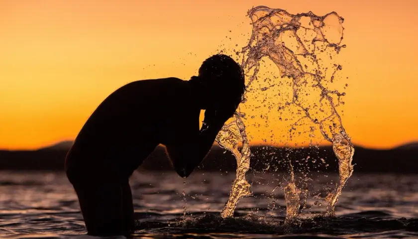 Silhouette of a person splashing water on their face at sunset.