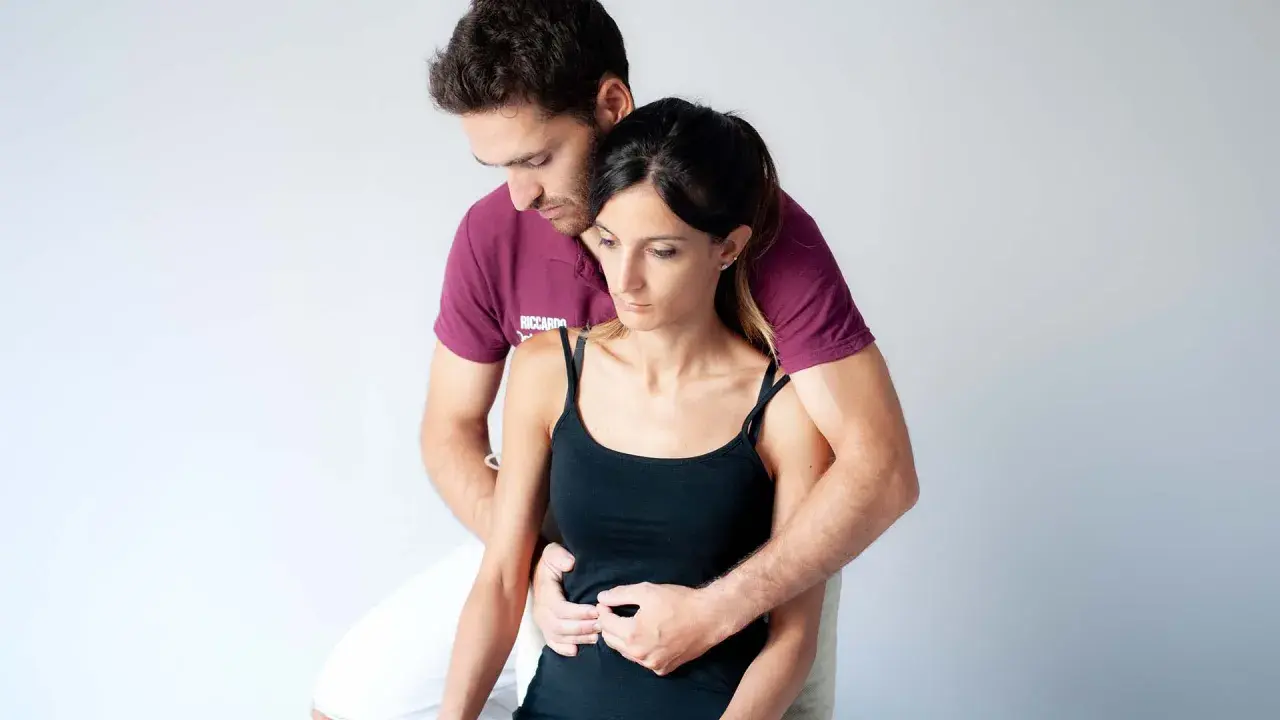 Un terapista esegue un massaggio diaframma su una donna, con le mani posizionate sull'addome per favorire il rilassamento e la respirazione profonda.