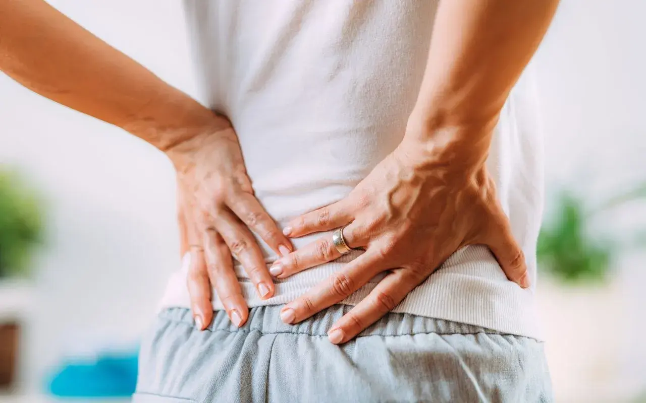 Mani che premono sulla schiena dolente, cercando sollievo nei punti shiatsu per sciatica.