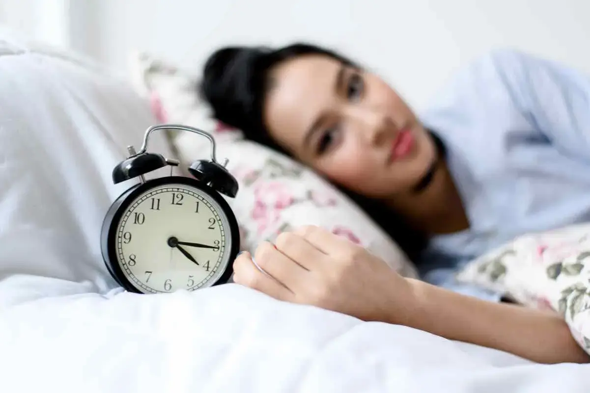 Svegliarsi alle 4 è un momento chiave per il benessere secondo la medicina cinese. La donna nella foto è a letto, con una sveglia che segna le 4.
