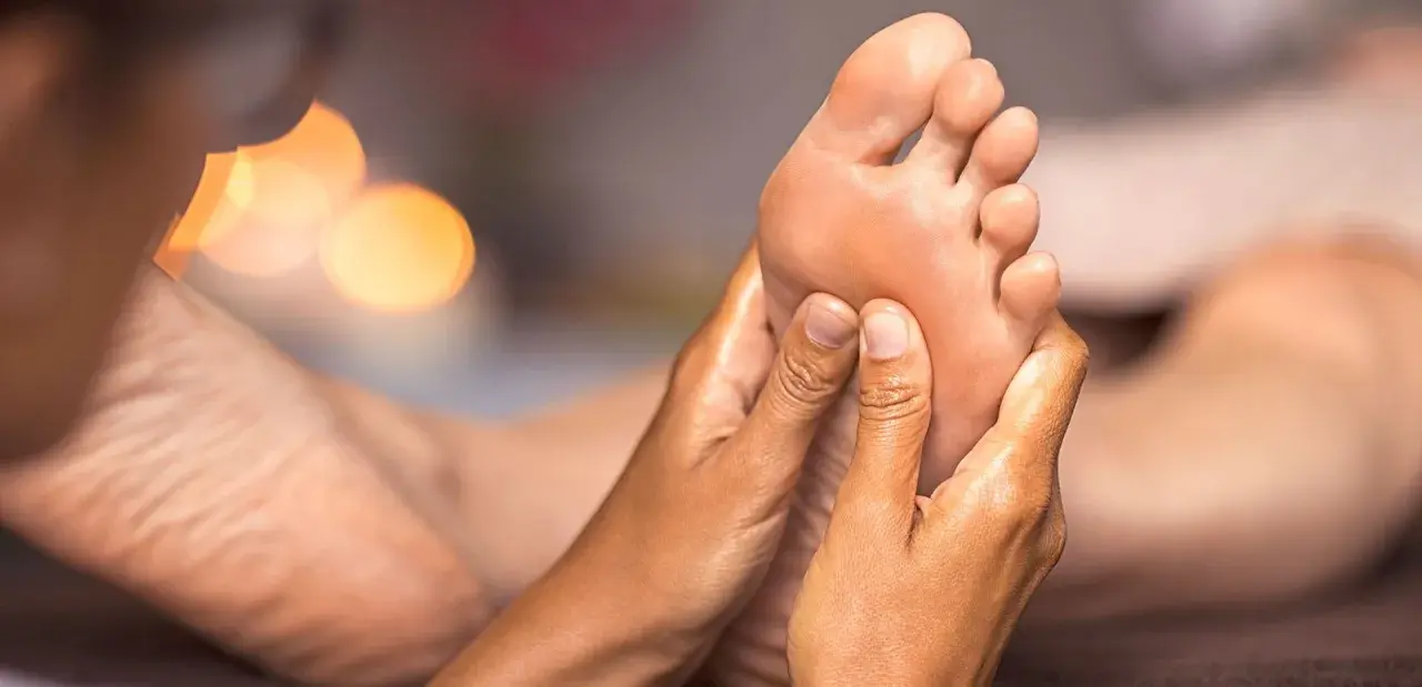 Close-up of hands massaging a foot, with soft, blurred lights in the background.