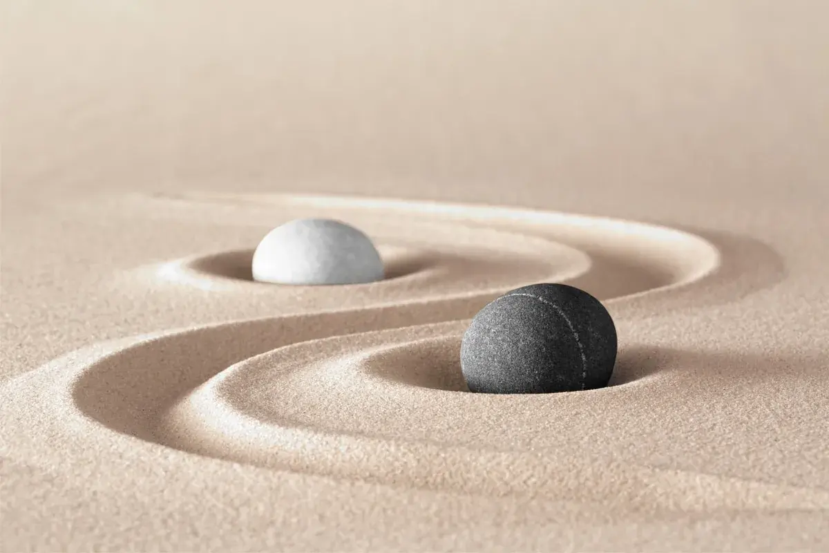 Due pietre, una bianca e una nera, su sabbia rastrellata, evocano il simbolo bianco e nero tao significato di equilibrio e dualità.