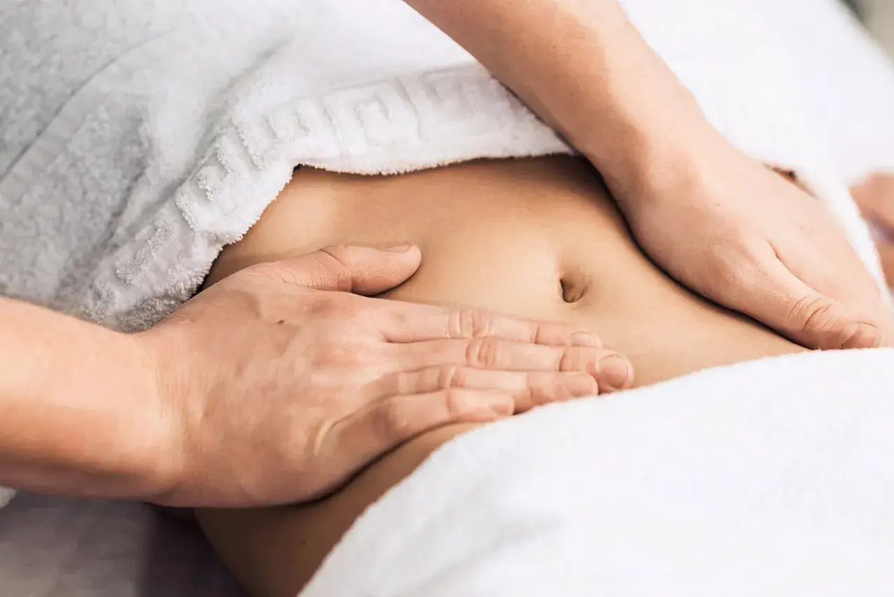 Hands massaging a person's abdomen, covered by a white towel.