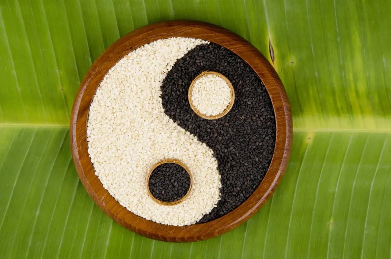 Semi di sesamo bianchi e neri disposti a formare il simbolo yin e yang, su una foglia verde.