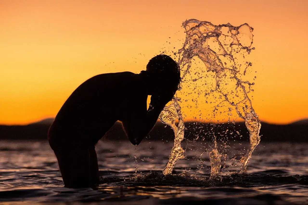 Silhouette of a person splashing water on their face at sunset.