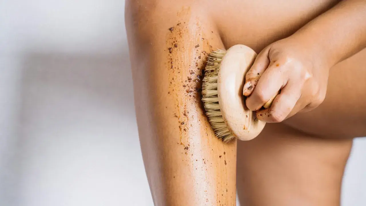 Mano che massaggia la gamba con uno scrub, dimostrando che i fanghi per cellulite funzionano per una pelle liscia.
