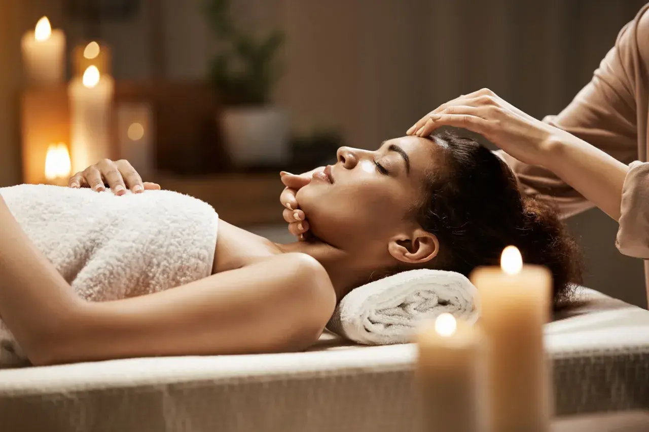 Woman receiving a facial massage in a dimly lit room with candles.