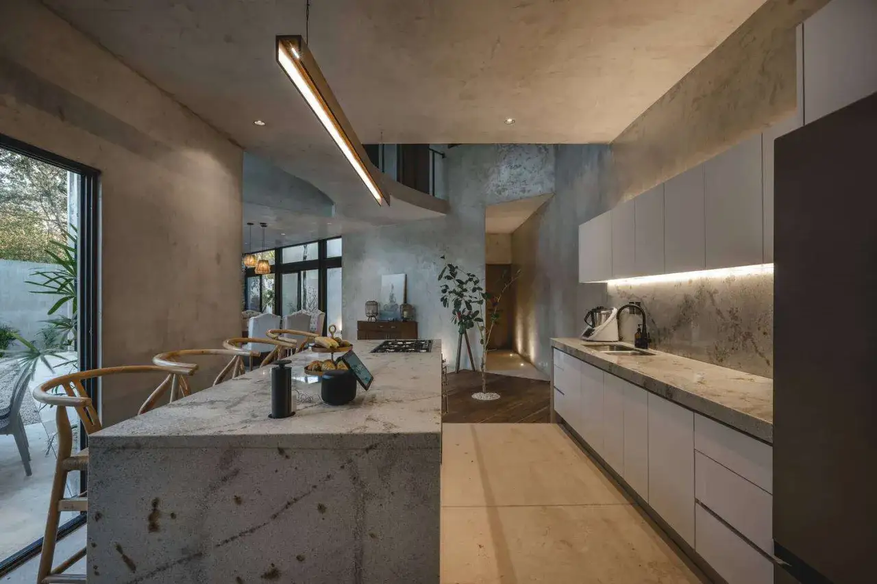 Cucina moderna con isola in pietra, sedie in legno e illuminazione soffusa. Un ambiente che favorisce il feng shui della persona, con materiali naturali e linee pulite.