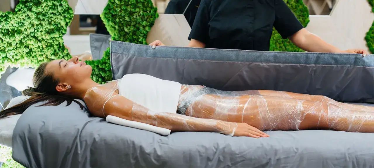 Donna avvolta in pellicola trasparente per un trattamento corpo. Si dice che i fanghi per cellulite funzionino per migliorare la pelle.