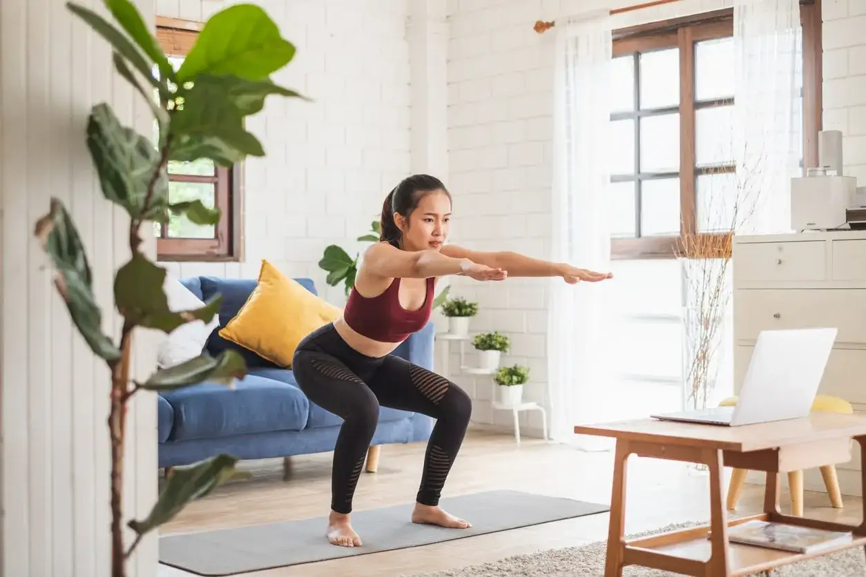 Donna esegue squat a casa, seguendo un tutorial su laptop, per rassodare il corpo.