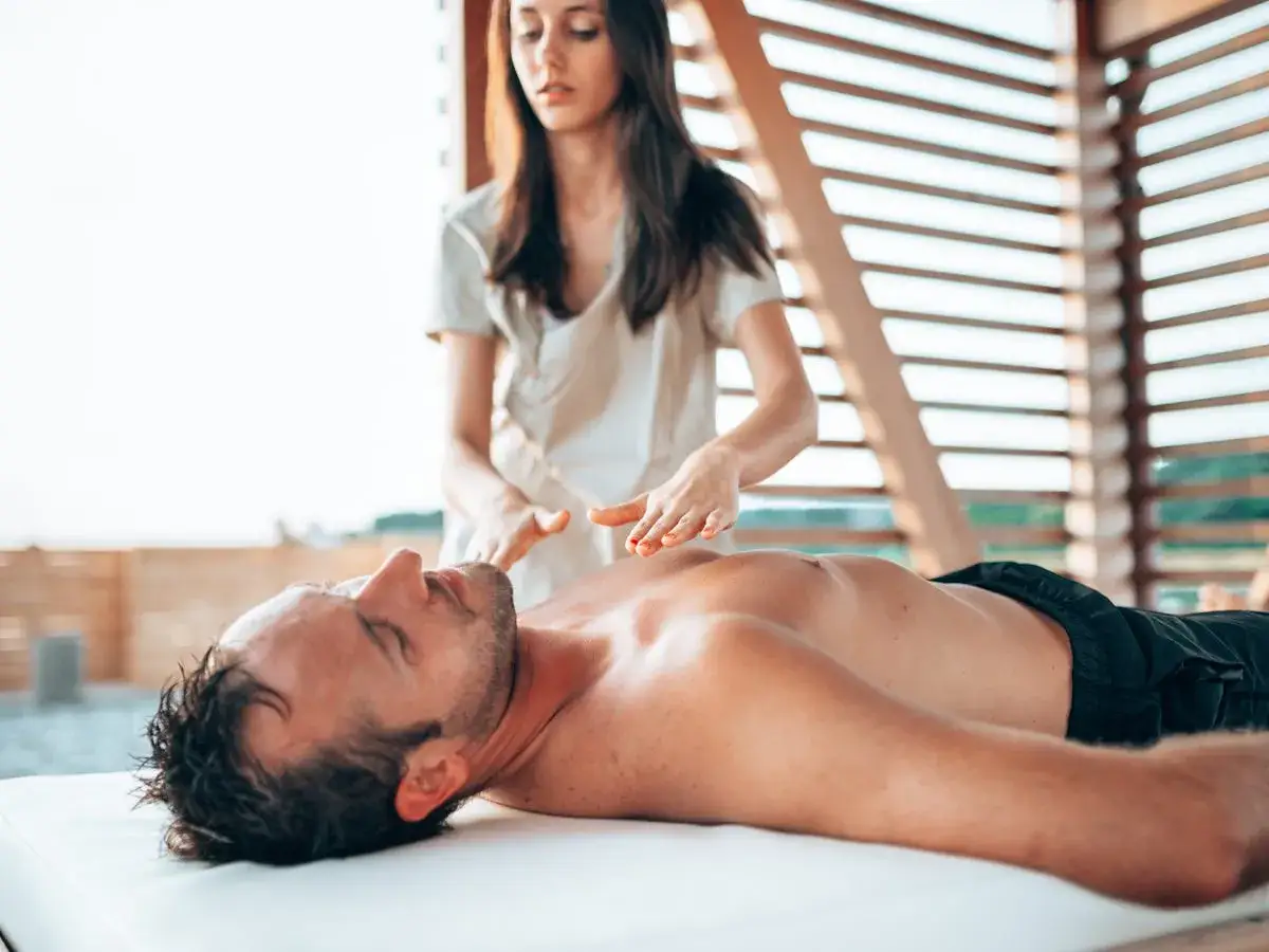 Donna esegue un massaggio addome uomo su un lettino all'aperto, con mani delicate che lavorano sul torace.