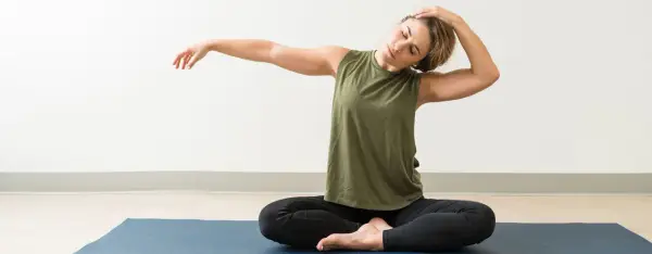 Donna in posizione yoga, con una mano dietro la testa, allungando il collo per rilassare i punti shiatsu cervicale.